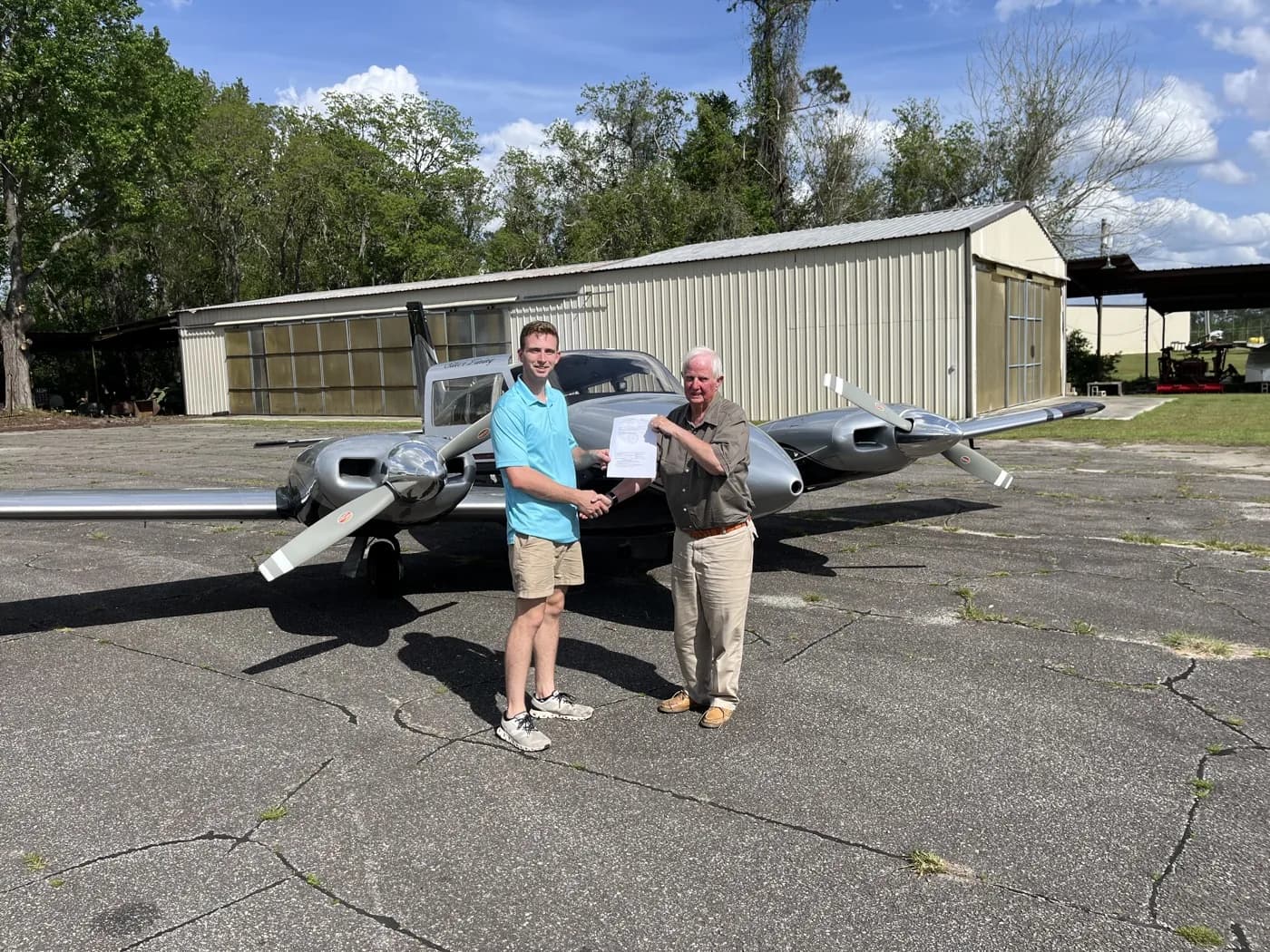 Instructor congratulating a Twin Comanche multi-engine student in front of the ACOM hangar at 71J