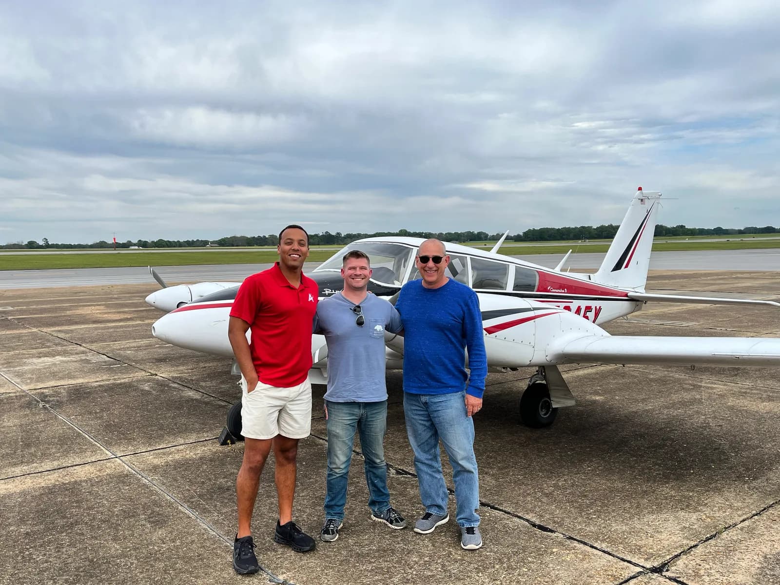 Three ACOM students celebrating with a Twin Comanche after multi-engine training