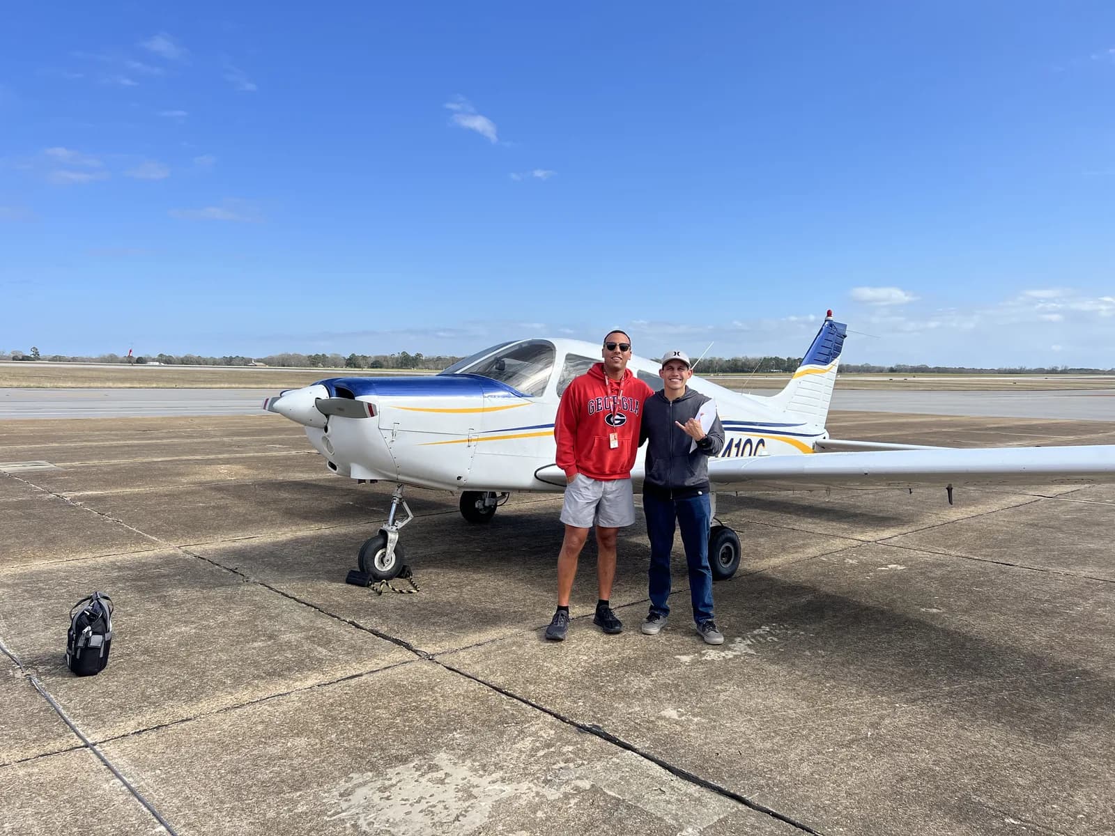 Two ACOM Aviation students celebrating with a Piper Cherokee on the ramp after their checkrides