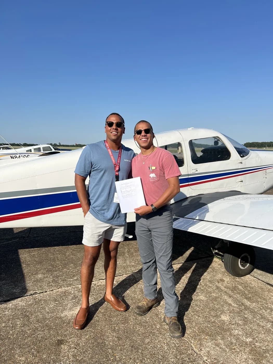 Two students holding a new pilot certificate in front of a red-white-and-blue Piper Cherokee at 71J