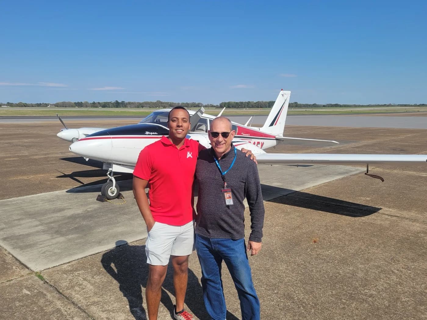 ACOM student in branded red shirt with instructor in front of a Piper Twin Comanche at Ozark-Blackwell Airport