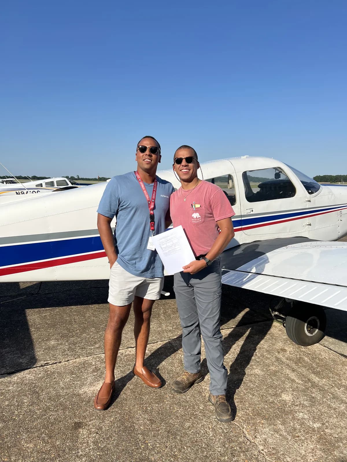 Two private pilot students celebrating with a Piper Cherokee after their checkride at 71J
